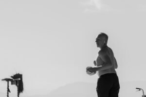 Dynamic monochrome image of an elderly man jogging along a beach, emphasizing fitness and lifestyle.